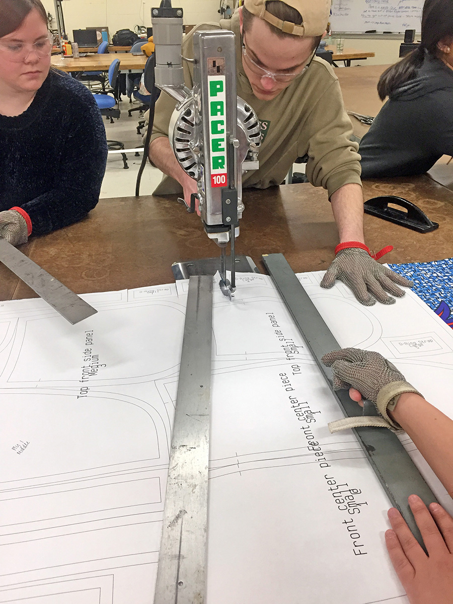 ​   UW-Stout students Amanda Nelson, at left, and Tyler Wagner use an electrical band saw to cut the pattern pieces for the skirts.  ​